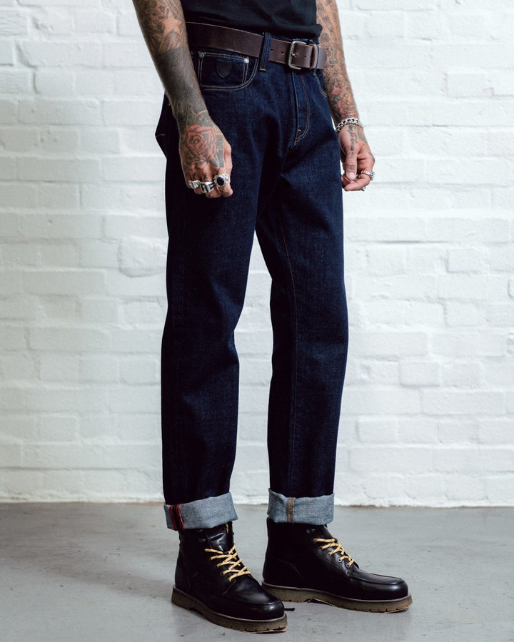 Person wearing dark jeans and black boots against a white brick wall.