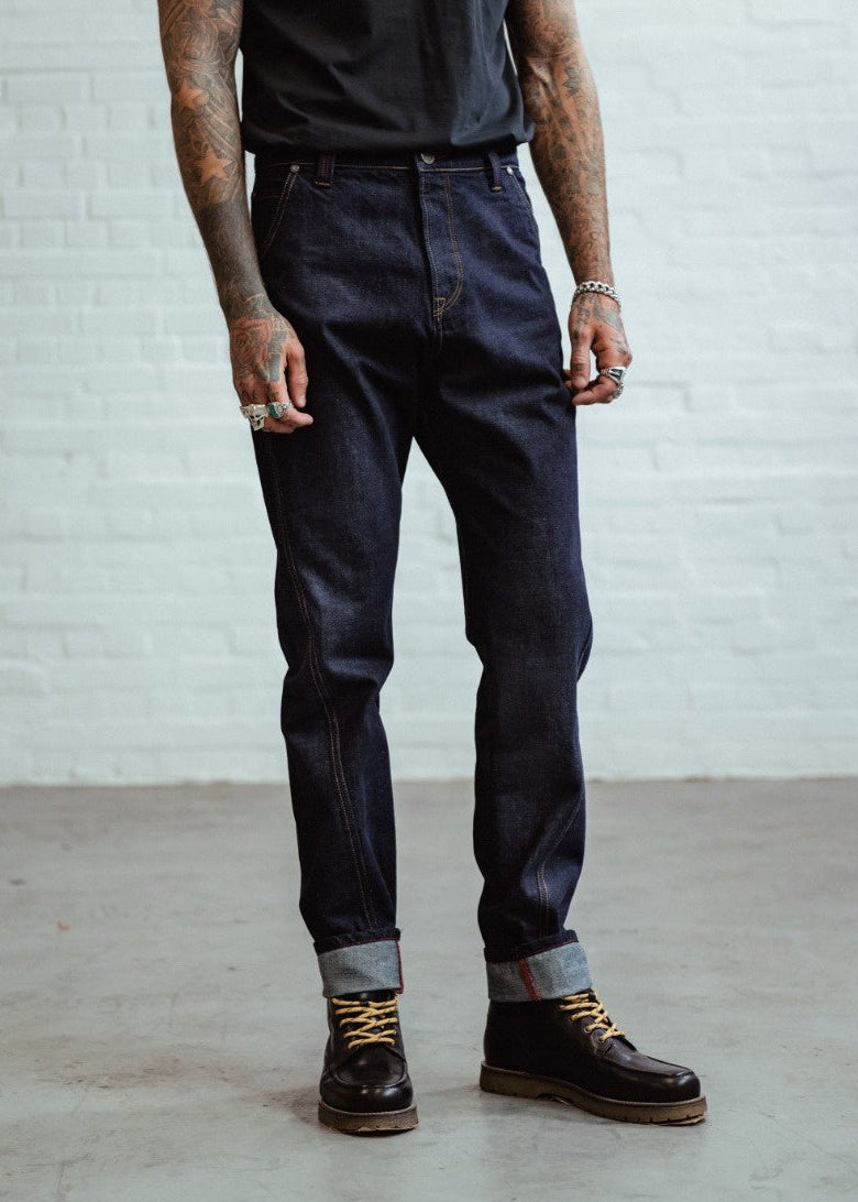 Person wearing dark blue jeans and black shoes against a white brick wall.